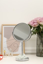 Mirror, perfumes and vase with pink roses on white dressing table