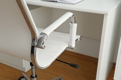 Photo of Modern office chair near table indoors, closeup. Stylish workplace interior