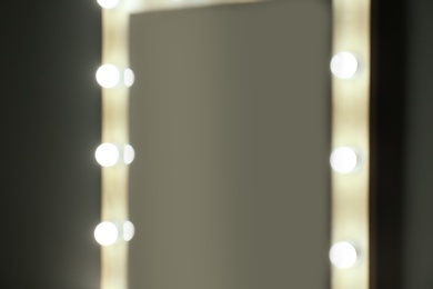 Blurred view of mirror with light bulbs on grey wall, closeup. Dressing room