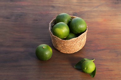 Photo of Fresh ripe limes in wicker basket on wooden table