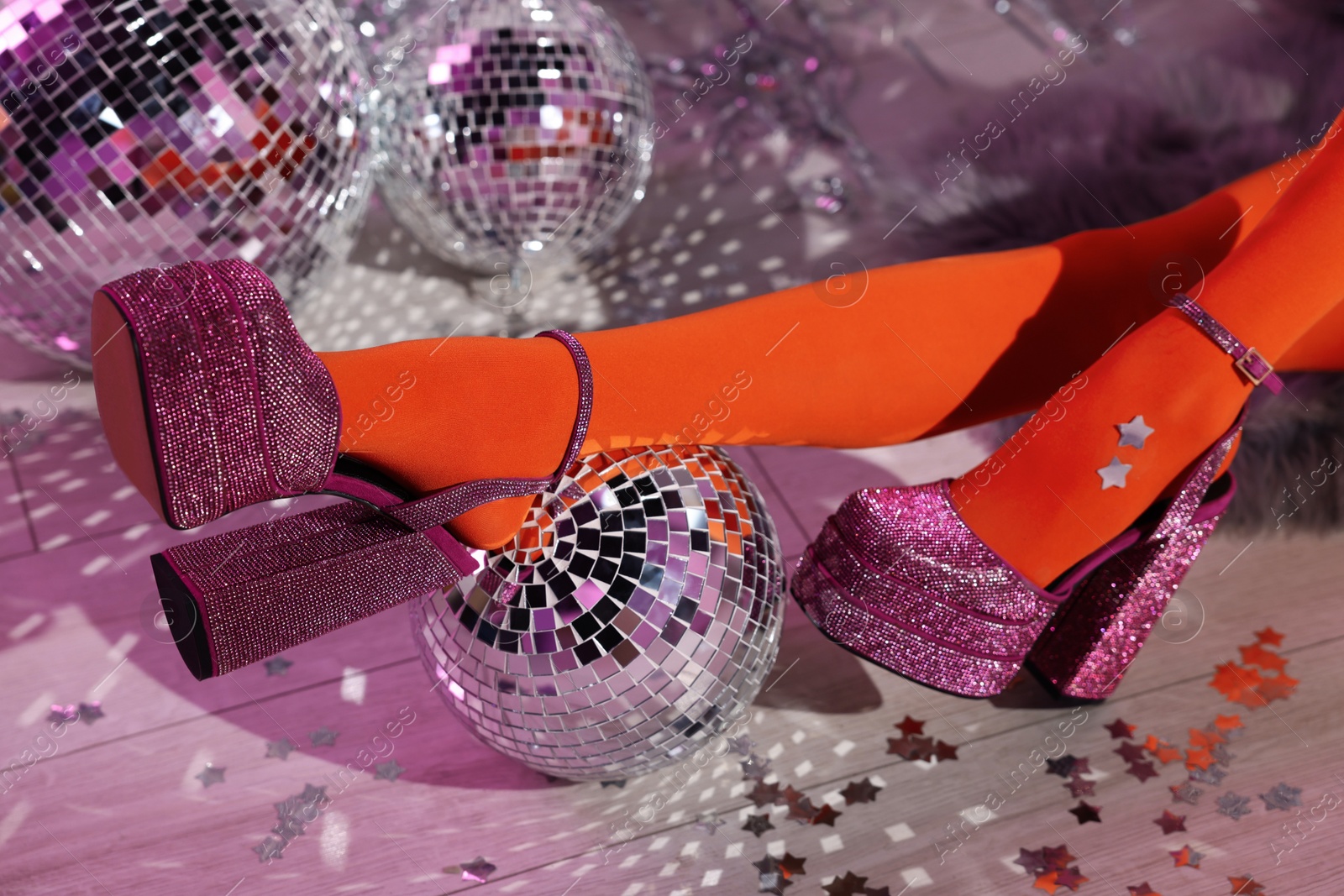 Photo of Woman in orange tights and pink high heeled shoes among disco balls indoors, closeup