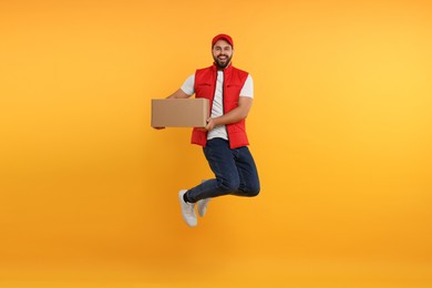 Photo of Happy young courier jumping with parcel on orange background