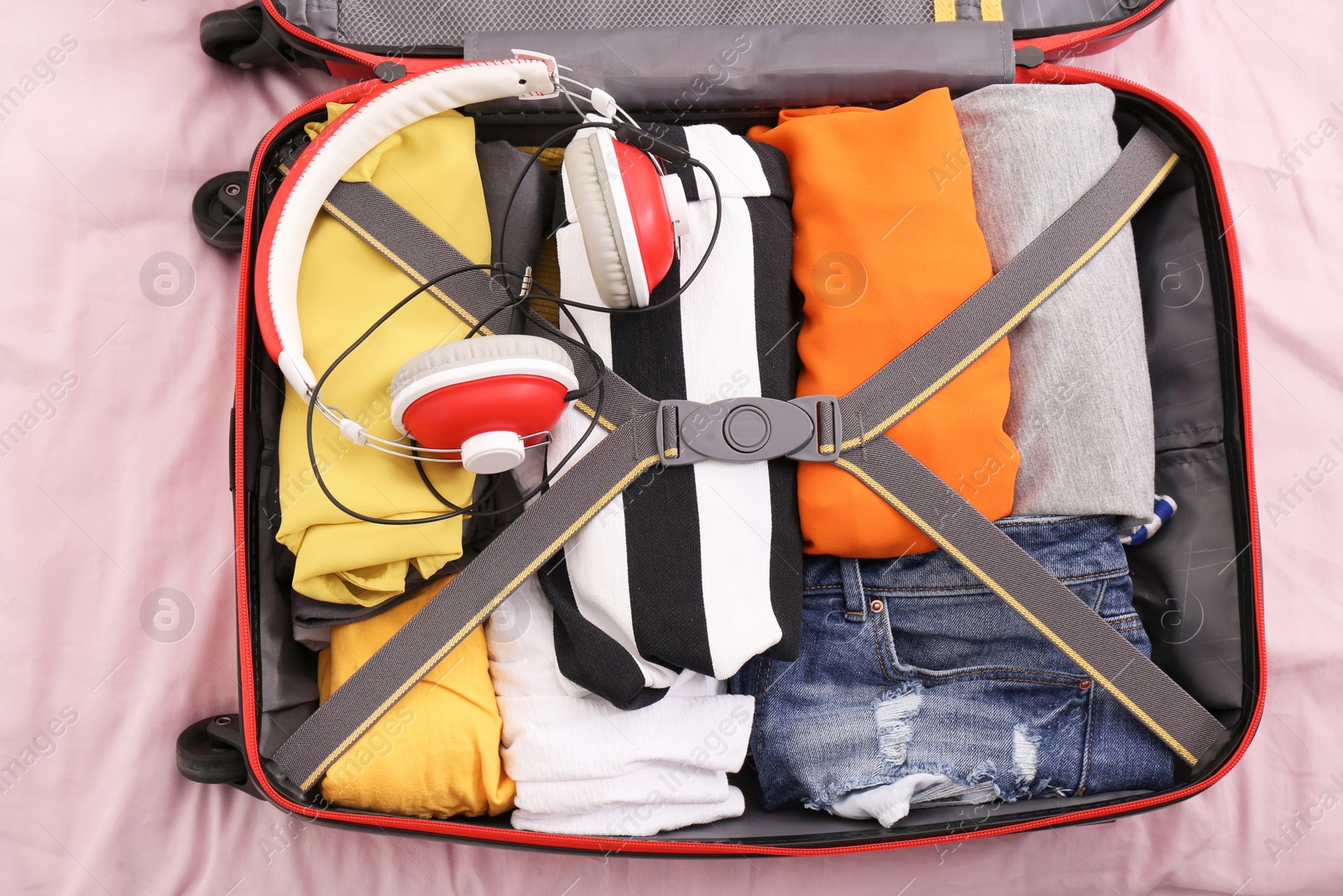 Photo of Open travel suitcase with packed things on bed, top view