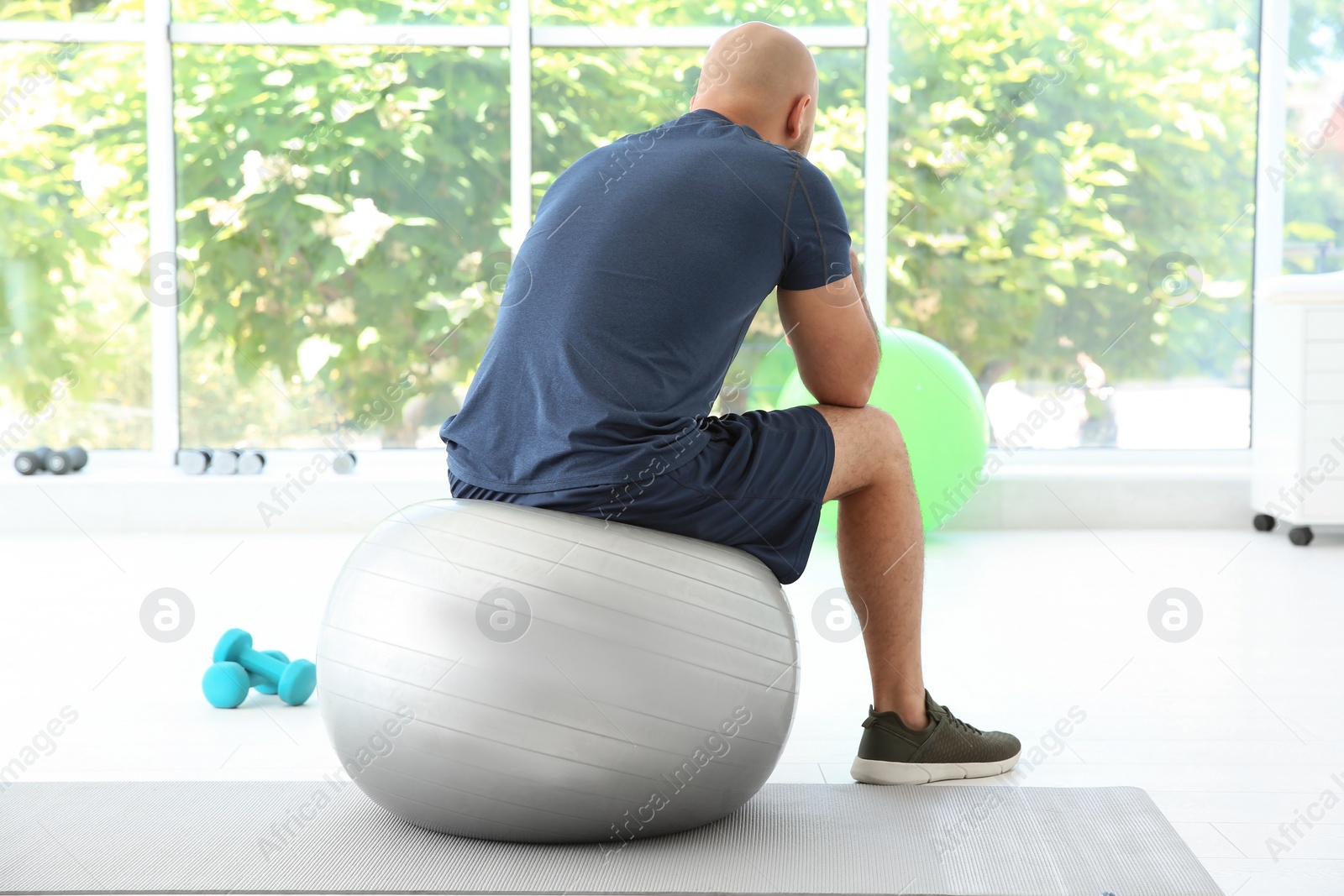 Photo of Tired overweight man sitting on fitness ball in gym