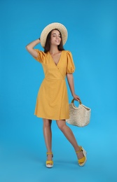 Young woman wearing dress with straw bag on light blue background