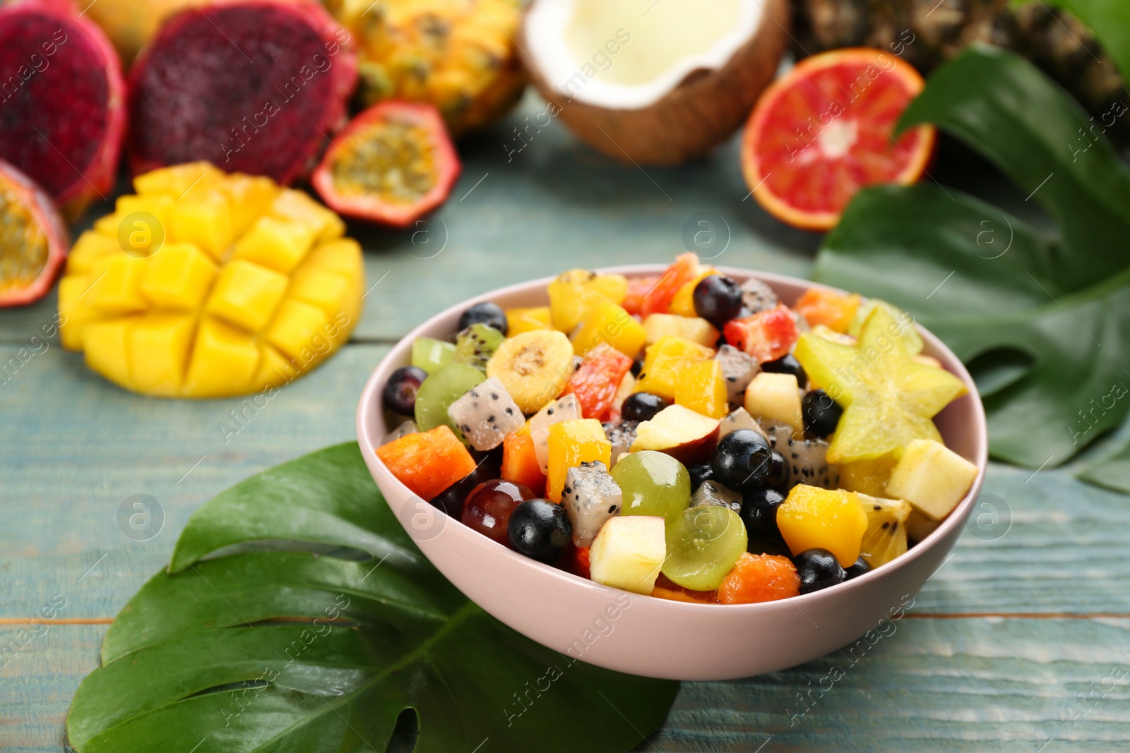 Photo of Delicious exotic fruit salad and ingredients on light blue wooden table