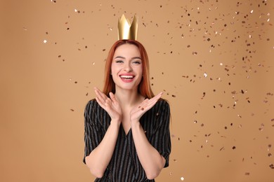 Photo of Beautiful young woman with princess crown under falling confetti on beige background