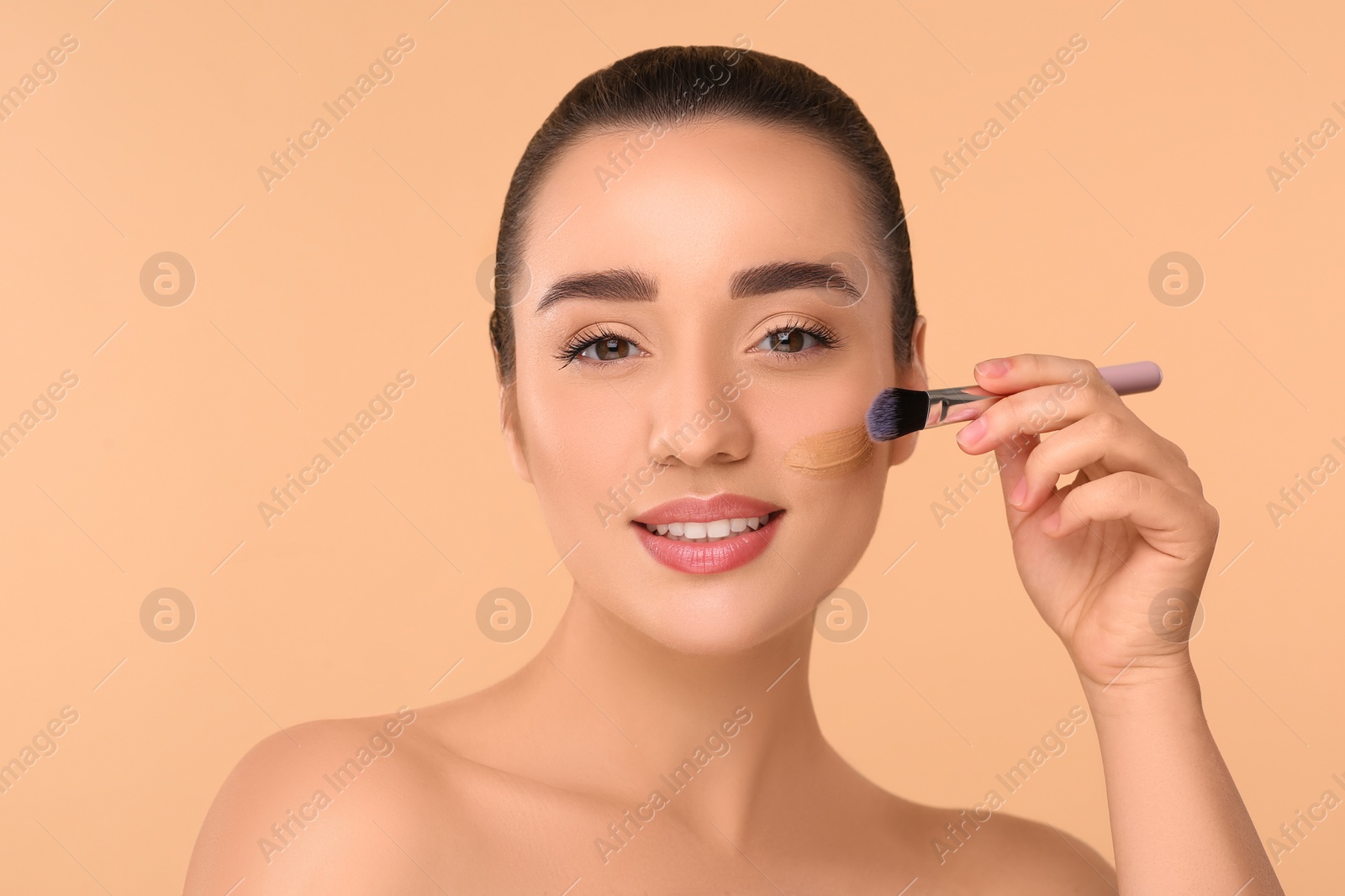 Photo of Woman applying foundation on face with brush against beige background