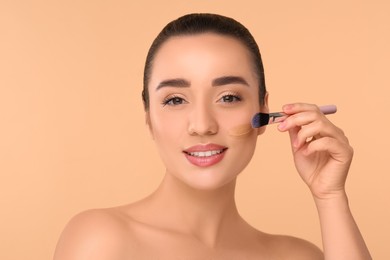 Photo of Woman applying foundation on face with brush against beige background