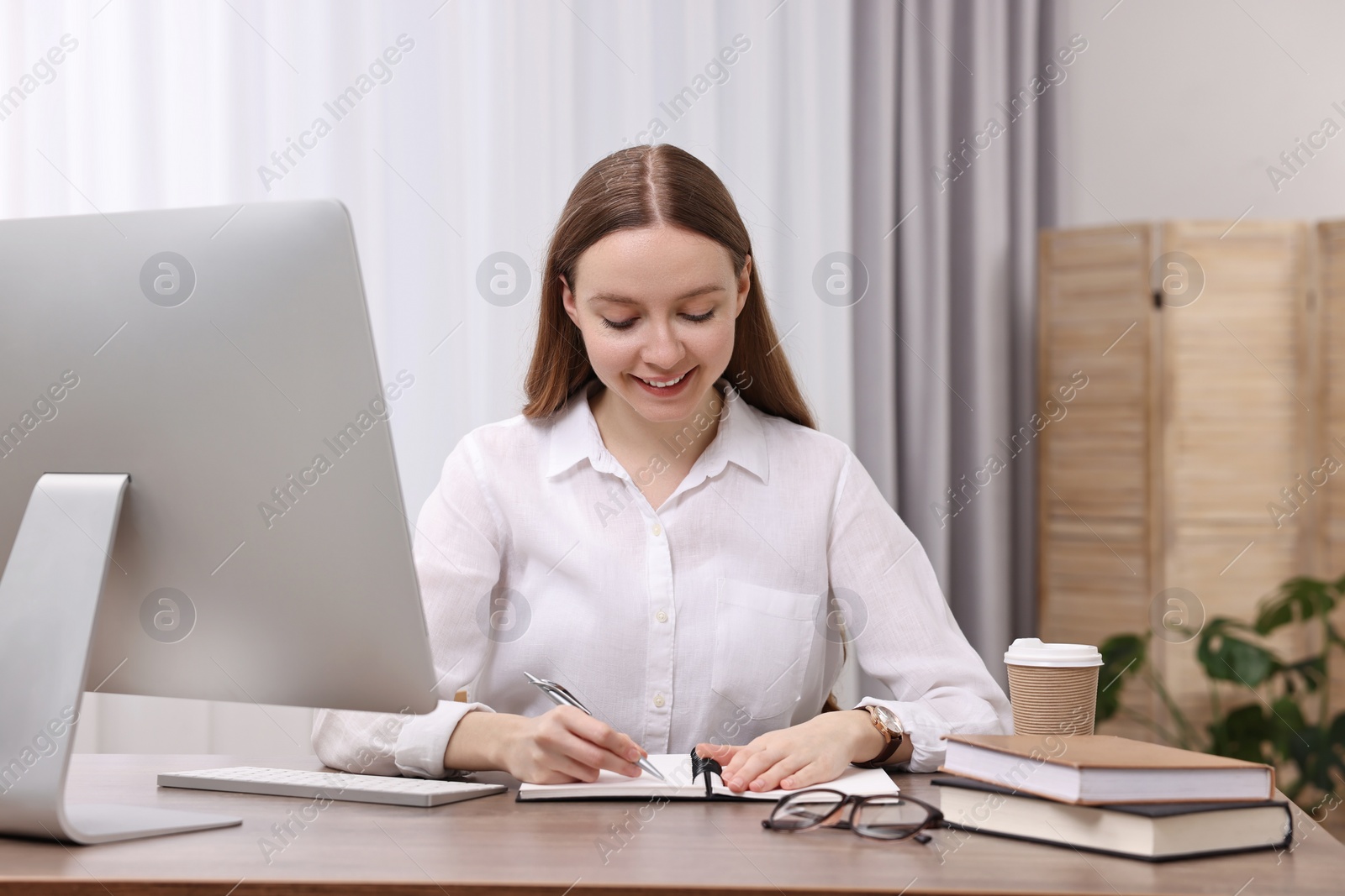 Photo of E-learning. Young woman taking notes during online lesson at wooden table indoors