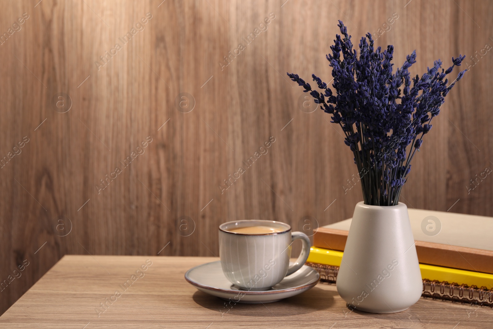 Photo of Bouquet of beautiful preserved lavender flowers, notebooks and cup of coffee on wooden table indoors, space for text