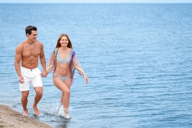 Happy young couple walking together on sea beach. Space for text