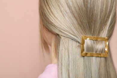 Young woman with beautiful gold hair clip on pink background, closeup