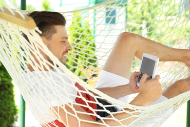 Photo of Man with tablet relaxing in hammock outdoors on warm summer day