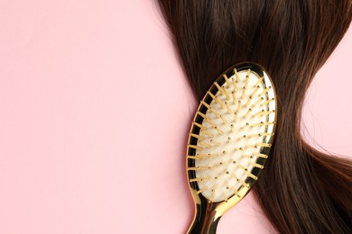 Stylish brush with brown hair strand on pink background, top view. Space for text