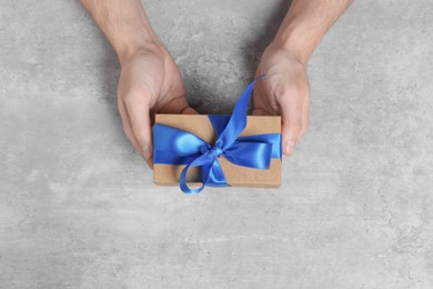 Photo of Man holding gift box with blue bow at grey table, top view
