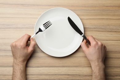 Man with empty plate and cutlery at wooden table, top view