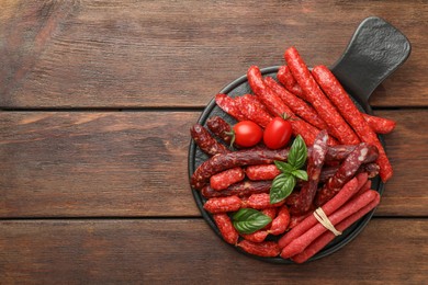 Photo of Different thin dry smoked sausages, basil and tomatoes on wooden table, top view. Space for text