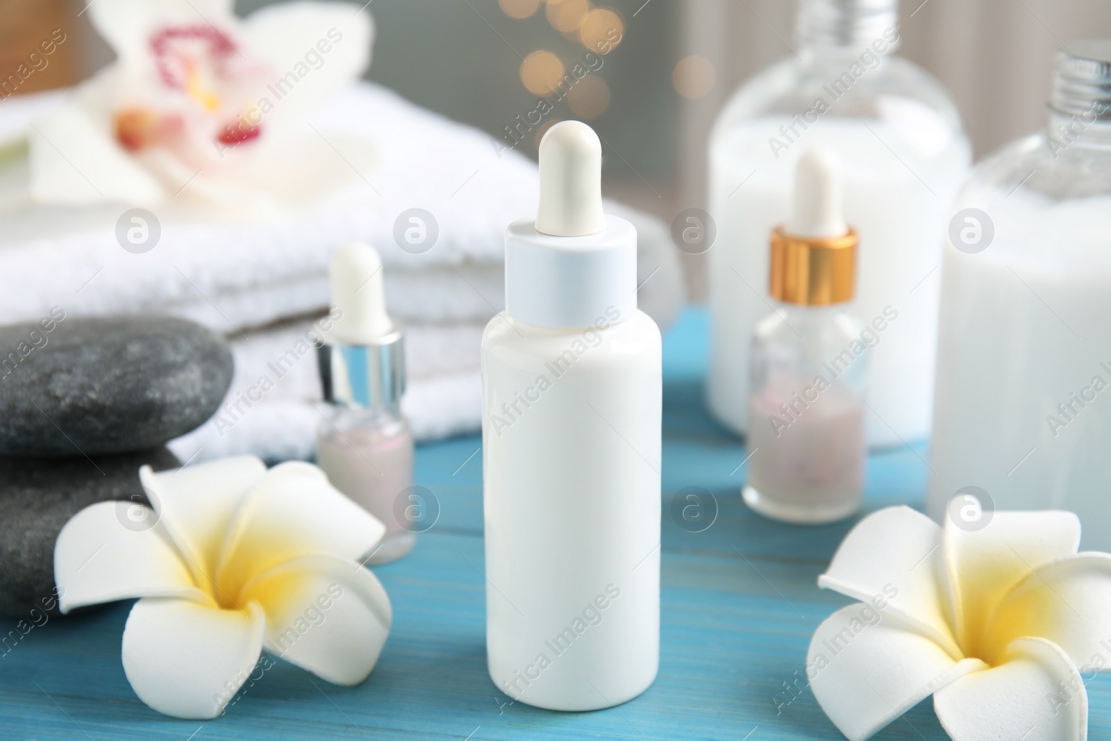 Photo of Beautiful spa composition with essential oil and plumeria flowers on turquoise table against blurred lights, closeup