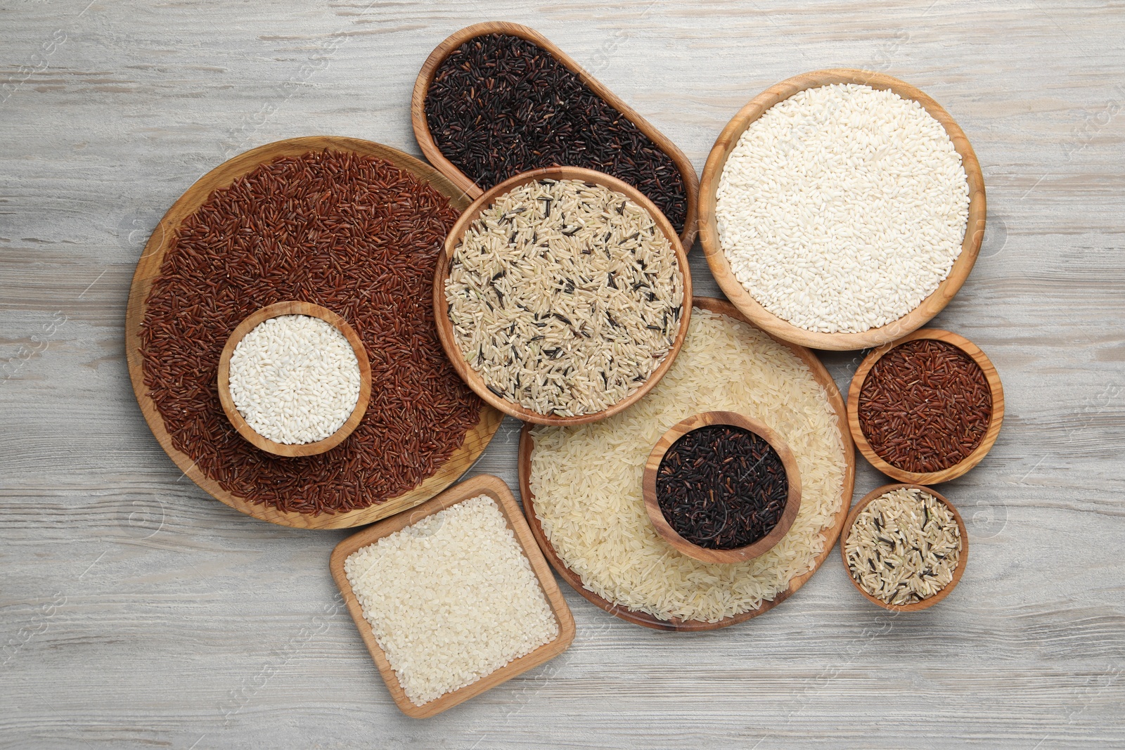 Photo of Dishes with different sorts of rice on white wooden table, flat lay