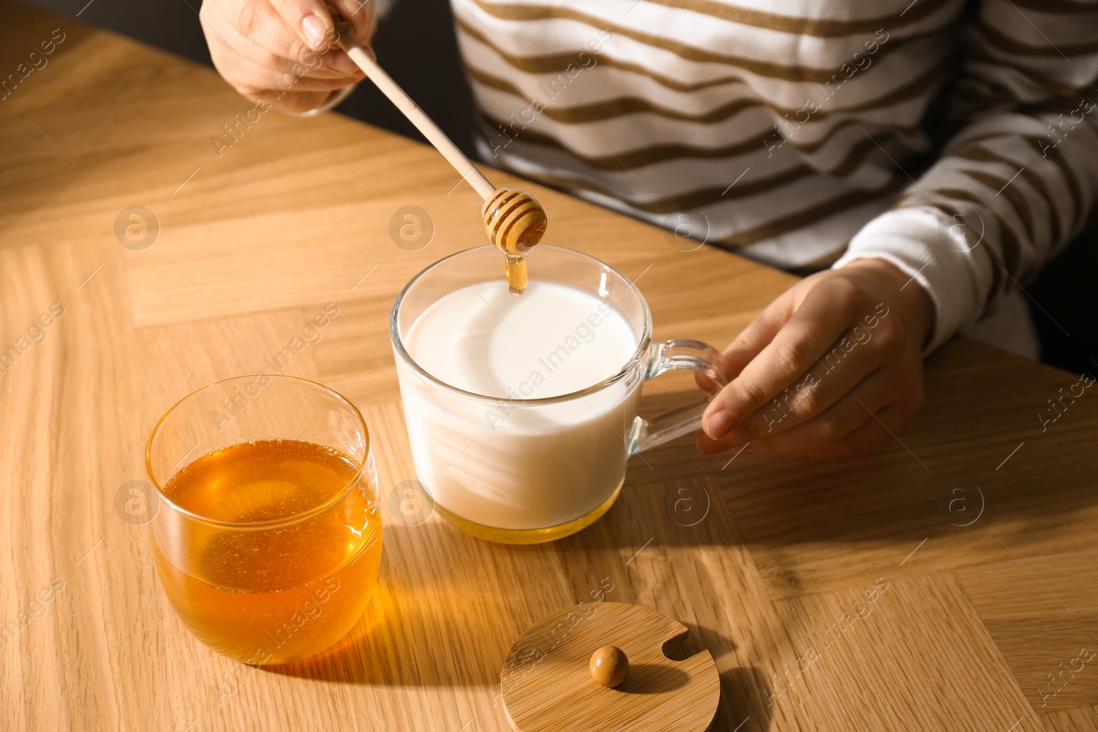 Photo of Woman adding honey to milk at wooden table closeup