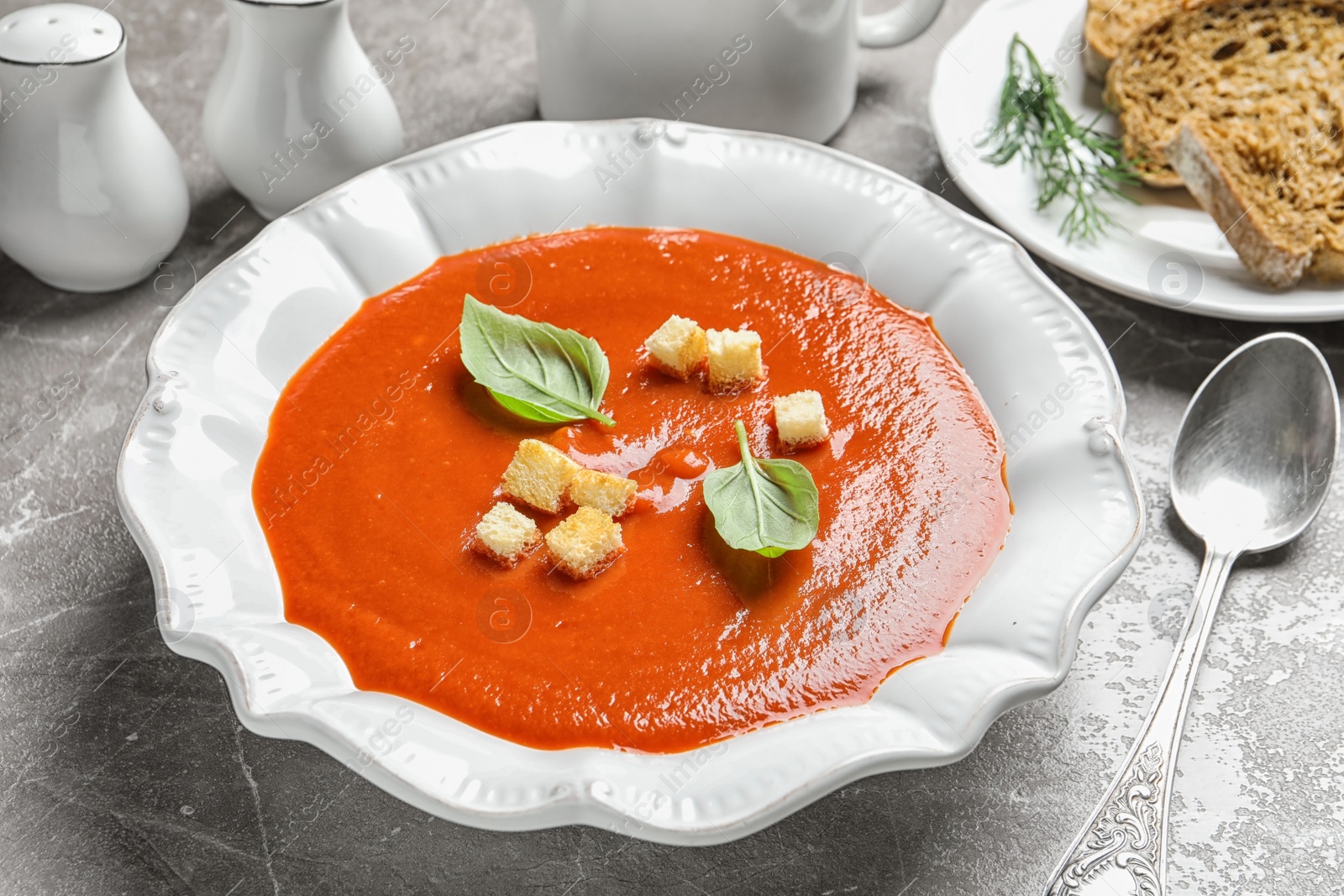 Photo of Fresh homemade tomato soup served with bread on grey table