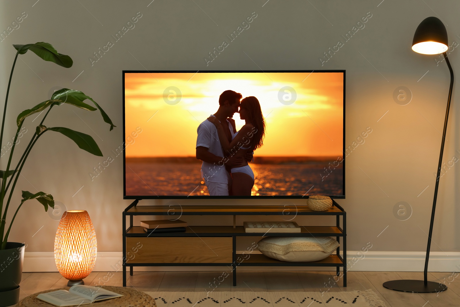 Image of Modern TV set on wooden stand in room. Scene of romantic movie on screen