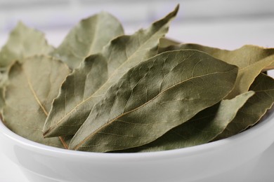 Photo of Dry bay leaves in white bowl, closeup