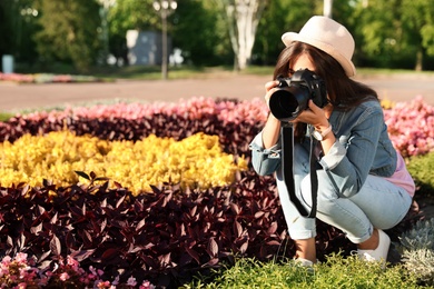 Young female photographer taking photo of flowers with professional camera outdoors