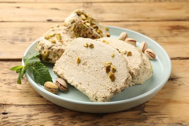 Photo of Tasty halva with pistachios and mint on wooden table, closeup