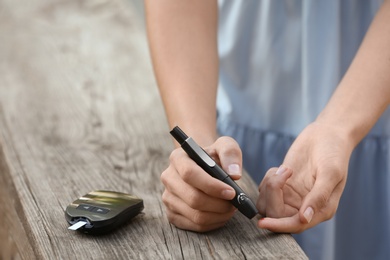 Photo of Woman using lancet pen near wooden surface outdoors. Diabetes control