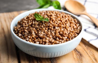 Bowl of buckwheat porridge with basil on wooden board