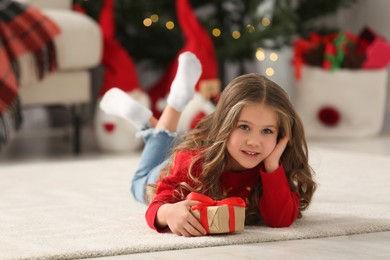 Photo of Happy girl lying on soft carpet with Christmas gift at home