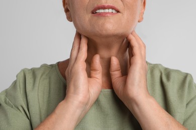 Photo of Mature woman doing thyroid self examination on light grey background, closeup
