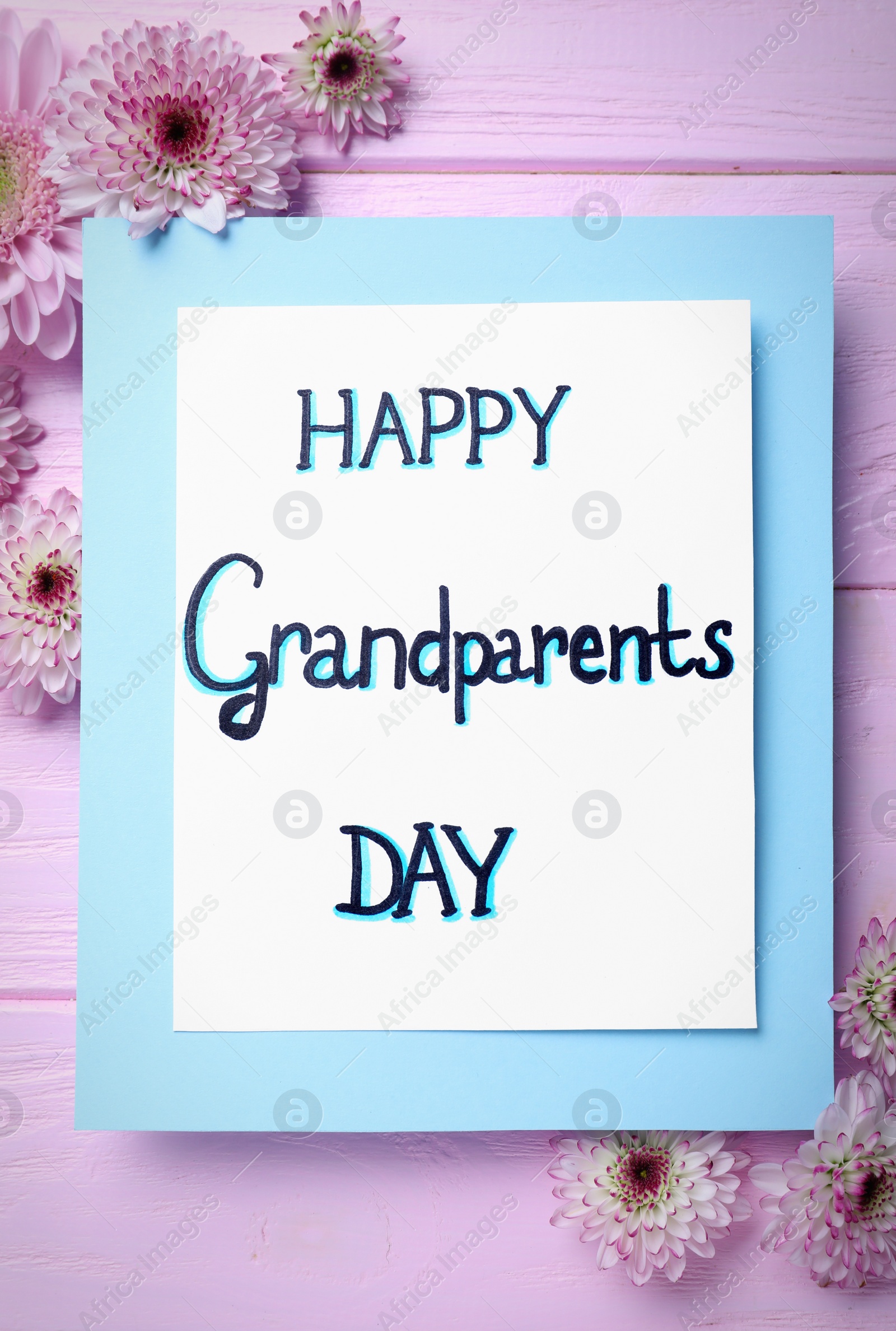 Photo of Beautiful flowers and card with phrase Happy Grandparents Day on pink wooden table, flat lay