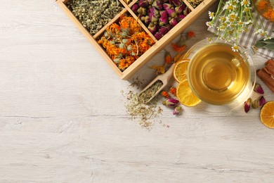 Photo of Freshly brewed tea and dried herbs on white wooden table, flat lay. Space for text