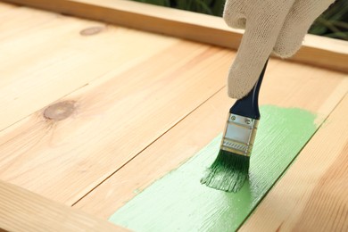 Photo of Worker applying green paint onto wooden surface, closeup. Space for text