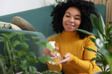 Happy woman spraying beautiful potted houseplants with water indoors