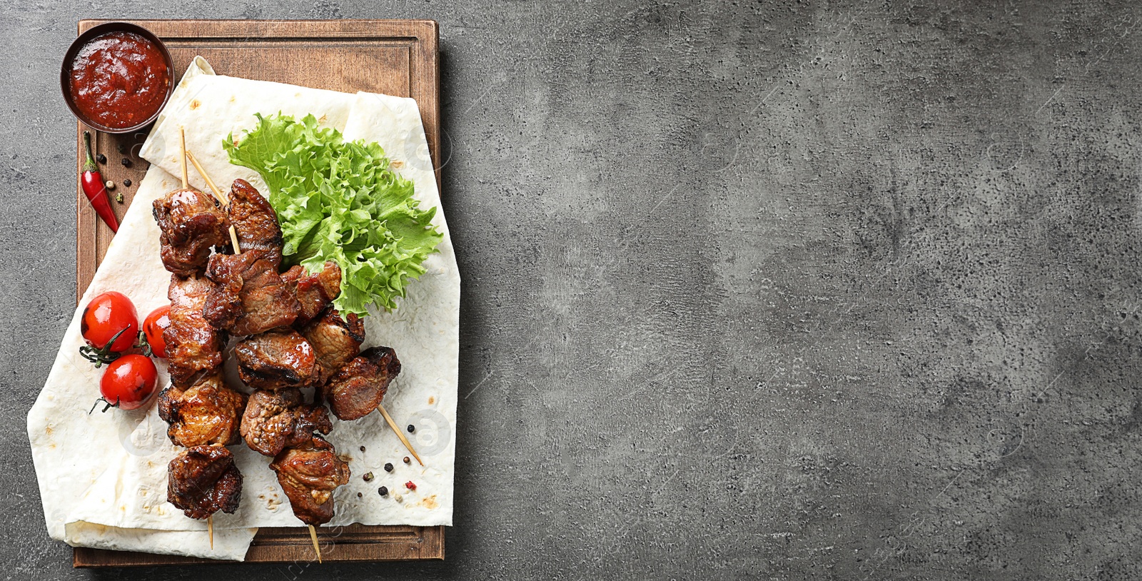 Image of Wooden board with delicious barbecued meat and space for text on gray table, top view. Banner design