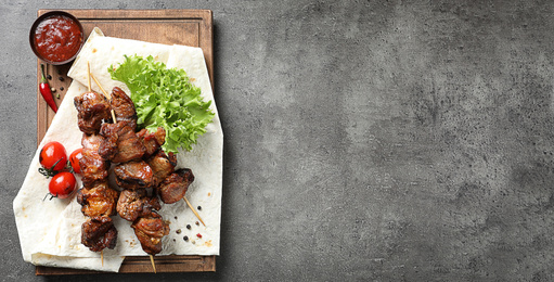 Image of Wooden board with delicious barbecued meat and space for text on gray table, top view. Banner design