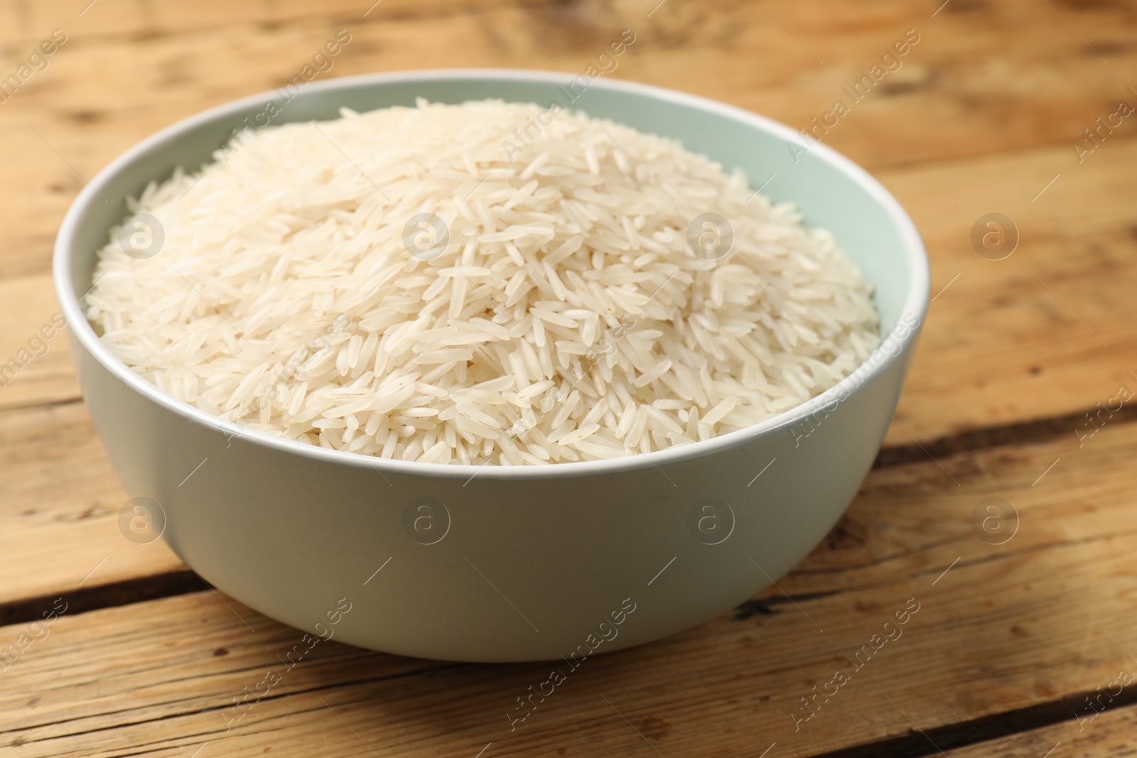 Photo of Raw basmati rice in bowl on wooden table, closeup