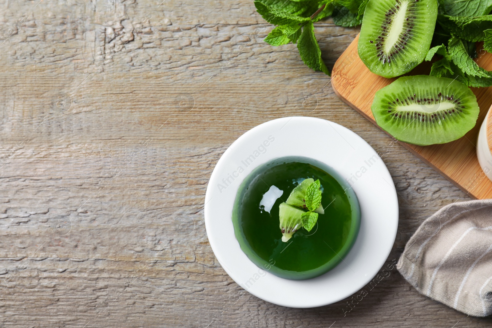 Photo of Delicious fresh green jelly with kiwi slices and mint on wooden table, flat lay. Space for text