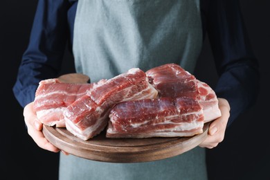 Photo of Woman holding wooden board with pieces of raw pork belly on black background, closeup