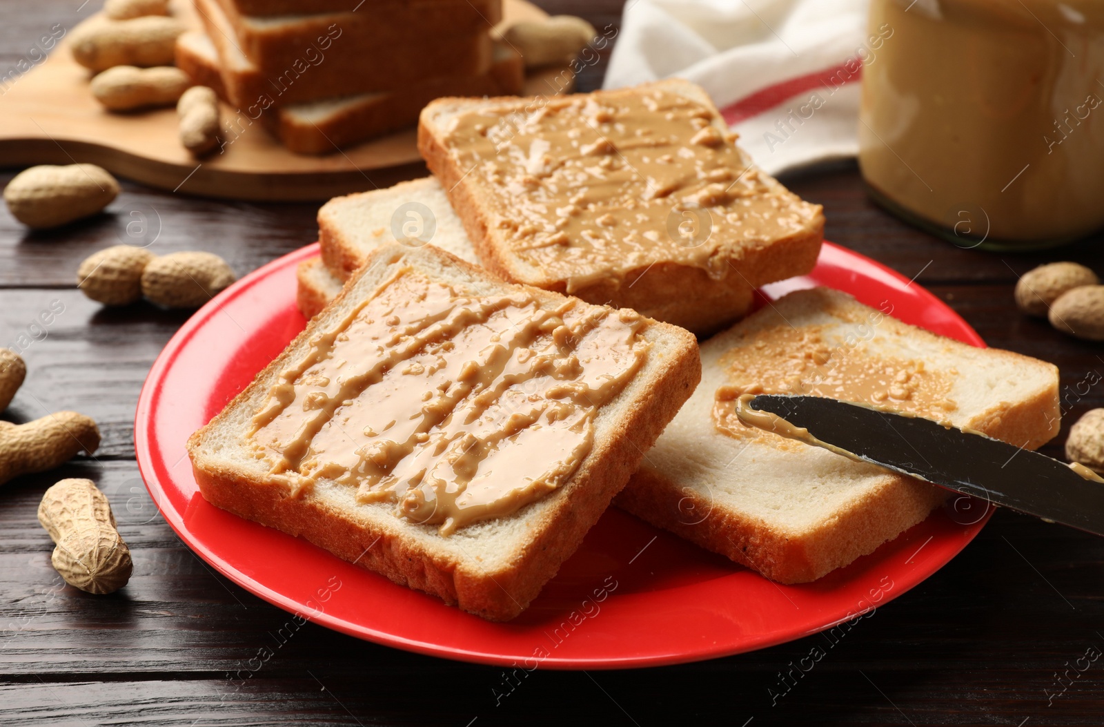 Photo of Delicious toasts with peanut butter, nuts and knife on dark wooden table, closeup