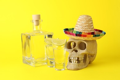 Human scull with Mexican sombrero hat, tequila and lime on yellow background