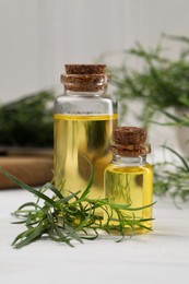 Photo of Bottles of essential oil and fresh tarragon leaves on white wooden table