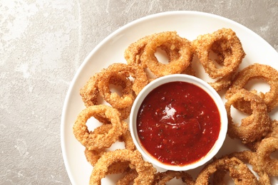 Photo of Homemade crunchy fried onion rings with sauce on color table, top view