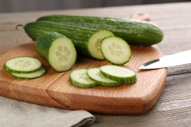 Photo of Cucumbers, knife and cutting board on wooden table, closeup