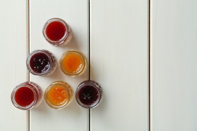 Photo of Jars of different jams on white wooden table, flat lay. Space for text