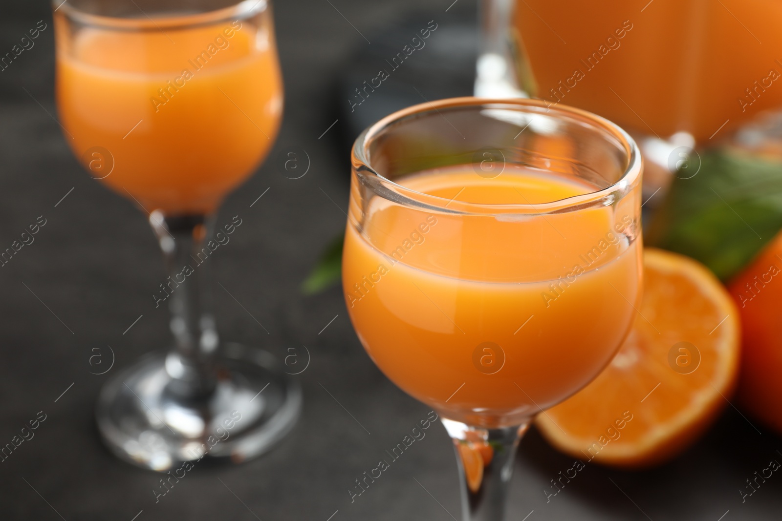 Photo of Delicious tangerine liqueur in glass on grey table, closeup